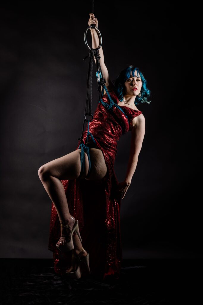 A woman in a red dress is suspended in blue rope